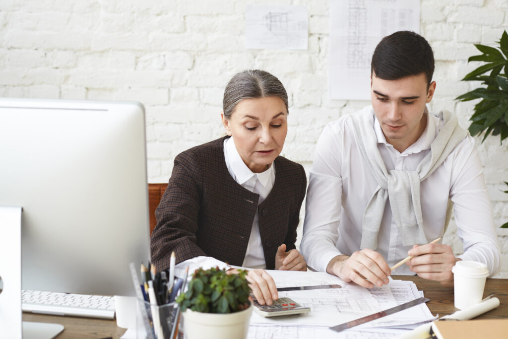 experienced-mature-woman-architect-with-gray-hair-sitting-her-workplace-with-young-focused-man-assistant-revising-drawings-project-documentation-using-calculator-check-measurements-scaled- Professional CPA services
